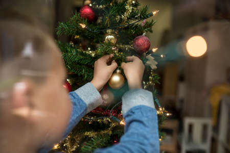 Rear view of a young boy decorating Christmas Tree with baubles behind glass window.の写真素材