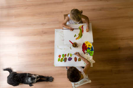 High angle view of two children painting on table with dog lying on floor.の写真素材