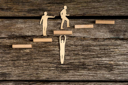 Teamwork concept using cut outs of paper men with one supporting steps, one giving a helping push from behind and the third walking forwards to success.の写真素材
