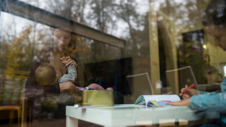 Young family inside the home viewed through the window with reflections on the glass with one child...