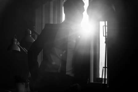 Businessman in a shadowy office with a bright white light flare coming in through a window over his backlit shoulder.の写真素材