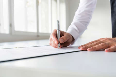 Businessman in white shirt signing contract, document or legal papers in a bright office.の写真素材