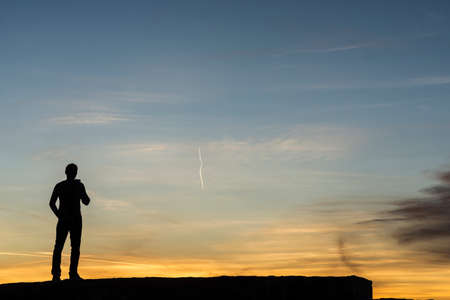 Man standing outdoors silhouetted against a colorful sunrise with copy space.の写真素材