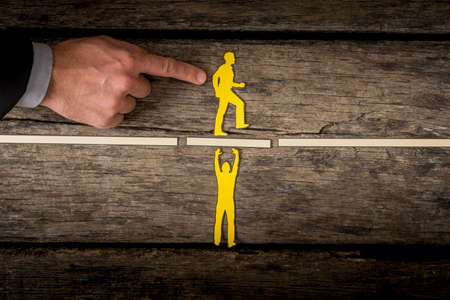 Man using his finger pushing small yellow paper figure onto white block being held up by other small yellow paper person.の写真素材