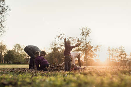Retro image of family rejoicing in an autumn sunset throwing leaves in the air in nature backlit by the glow of the sun.の写真素材