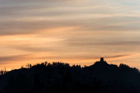 Old building on a forested mountain silhouetted against the fiery glow of the sun in a dark brooding sky with copy space.の写真素材