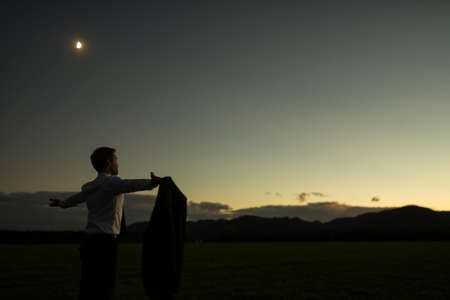 Businessman with removed jacket with his arms outspread standing in nature during sunset time.