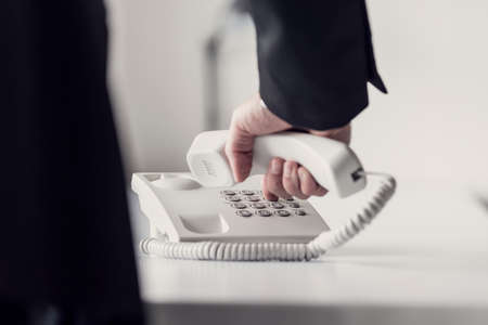 Retro toned image of a businessman dialing telephone number on a classical white landline telephone, low angle view between his arm and body.の写真素材