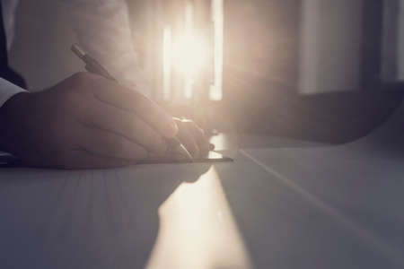 Designer drawing with a pen and ruler at an office table with sun flare from a window behind him, vintage effect toned image.の写真素材