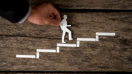 Paper silhouette cutout of a man and a human hand in business suit helping him climb the stairs over rustic wood.の写真素材