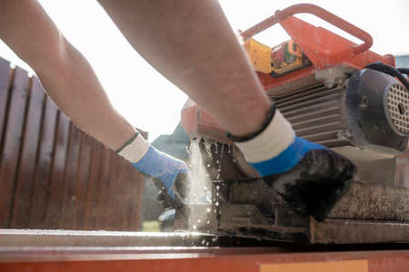 Close up on the hands of a man from behind using an angle grinder or circular saw outdoors to cut...