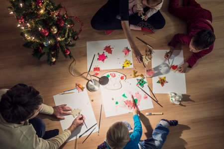 Top view of a family with two kids and a baby making Christmas decorations kneeling in a circle on...