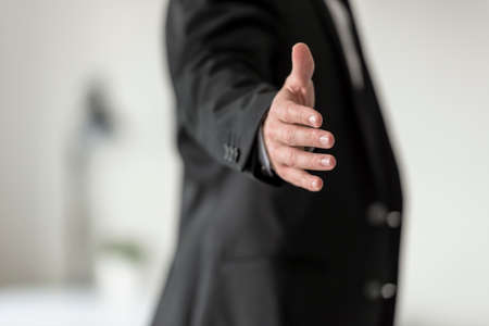 Businessman in black business suit standing in profile offering you a handshake.の写真素材