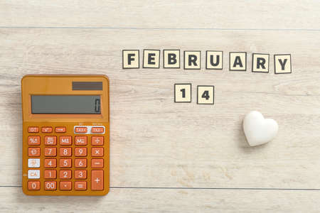 Calculator with 14 February Valentines date and a small white heart on a light colored wood background with copyspace.の写真素材