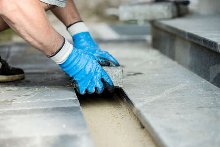 Contractor laying new paving bricks or stones, close up view of his gloved hands.の写真素材