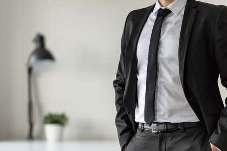 Business man in his office with his hands in the pockets of his suit pants in a close up view.の写真素材