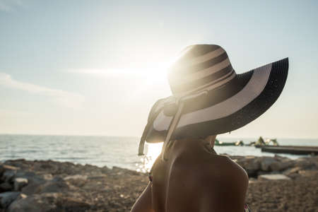 Rear view of woman in swimsuit at the beach watching sunset over sea with a bright light flare from behind.の写真素材