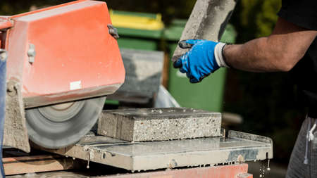 Building contractor working with a concrete block and an angle grinder, closeup view of his hands...