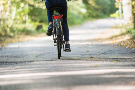 Rear cropped view of a woman riding a bicycle on a path outdoors as a recreational cardio training.