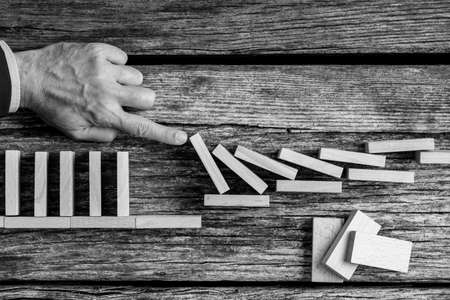 Conceptual monochrome image of the hand of a man avoiding collapse by stopping the destructive domino effect of wooden blocks.の写真素材