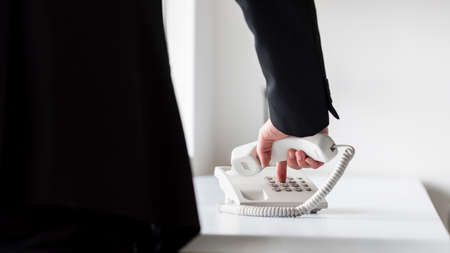 Businessman dialing telephone number on a classical white landline telephone, low angle view between his arm and body.の写真素材