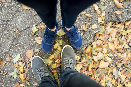 Couple standing amongst dried autumn or fall leaves in a first person perspective looking down at their feet.の写真素材