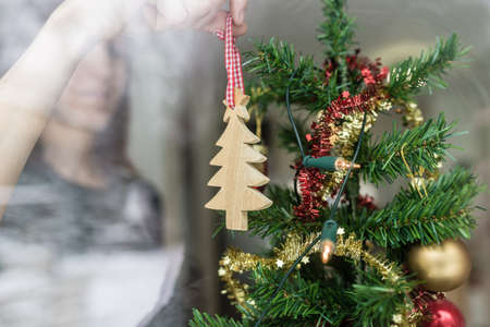 Woman putting up Christmas ornament at home holding a wooden tree in her hand seen through window...