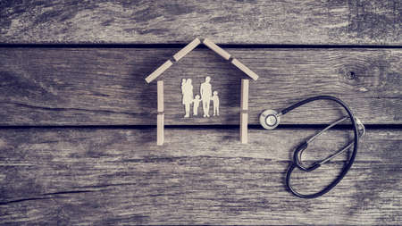 Cut outs of a family with kids in a house with a stethoscope lying on a wooden table alongside in a conceptual image.の写真素材