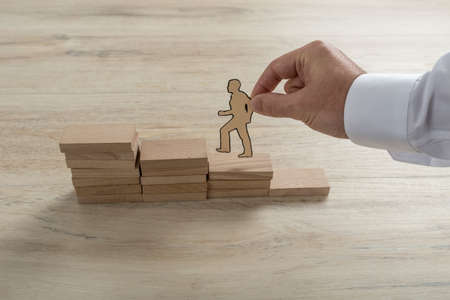 Businessman climbing the steps to success with paper silhouette cutouts of a man and a human hand helping him climb.の写真素材