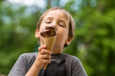 Outdoor portrait of young boy eating ice cream in crispy cone.の写真素材