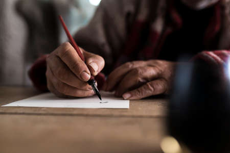 Close up view of a man with dirty hands writing on a sheet of paper with old fountain pen. の写真素材