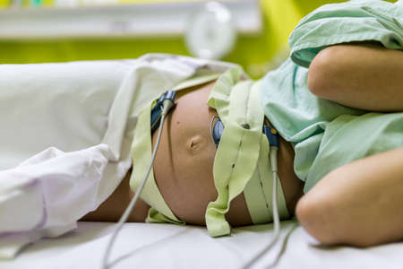 Pregnant woman undergoing cardiotocography to monitor the contractions of the uterus during childbirth.の写真素材