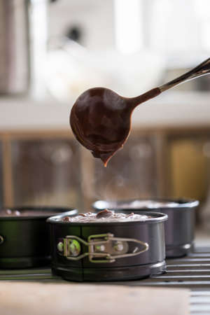 Baking tins with chocolate cake mix spooning it in with a ladle in a close up view.の写真素材