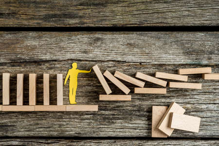 Single man holding up falling wooden bricks in a conceptual image of a paper cutout silhouette on a...