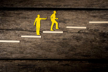 Cut outs of yellow paper men with one  giving a helping push from behind and the other one climbing the stairs.の写真素材