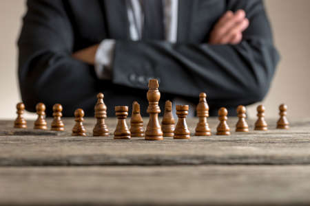 Man wearing suit sitting with folded arms in front of dark chess pieces at table .の写真素材