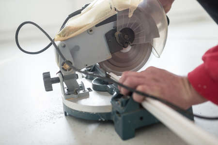 Laborer using a small electric circular saw to cut a length of plastic profile with focus to the...