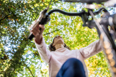 Woman riding a bicycle in autumn in a low angle view looking straight up at the handlebars and autumn trees.の写真素材
