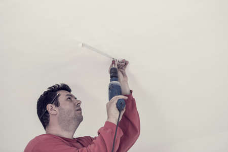 Retro effect faded and toned image of electrician using an electric drill to drill a hole in the ceiling of a building.の写真素材