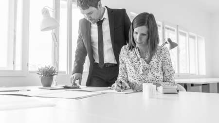 Two business partners, a young man and woman, working together on paperwork at a large office table viewed low angle.の写真素材