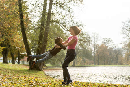 Happy fit young mother playing with her son at the edge of a lake in autumn swinging him around in her arms as she twirls.の写真素材