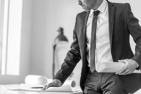 Greyscale image of a businessman or expert writing observations while working at the plan of a difficult project in the officeの写真素材