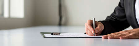 Wide panorama view of businessman hand signing legal or insurance document or business contract on white desk.の写真素材