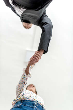 Businessman in a suit shaking hands with a woman in jeans in a view from directly below their hands with copy space on the ceiling.の写真素材