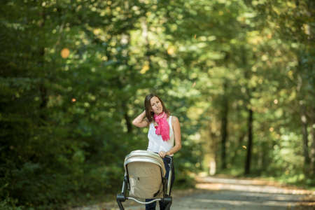Woman pushing baby carriage in park shot from low angle from the front with lots of foliage in...