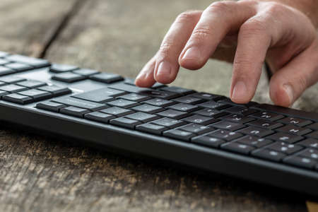Closeup of the hands of a man typing on a black keyboard as he enters information in an online communication concept.の写真素材