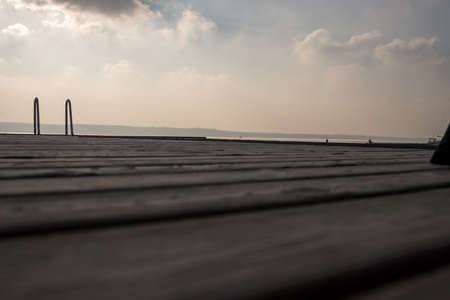 Wooden pier on the seashore against sky with sun behind clouds at dawn.の写真素材