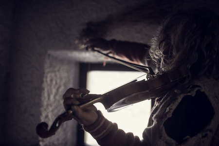 Black and white artistic image of and older man playing violin enthusiastically indoors next to a window.の写真素材