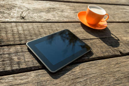 Blank digital tablet and coffee cup on a rustic wooden table.の写真素材