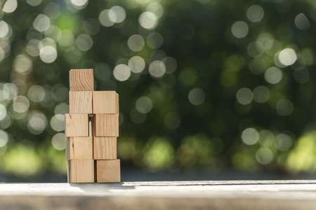 Stacked blank wooden toy blocks on a garden table outdoors against green with sparkling bokeh of sunlight in a conceptual image.の写真素材